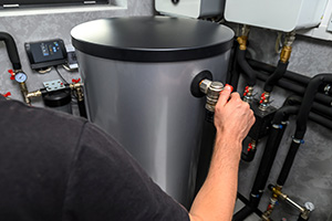 person adjusting a valve on a cylindrical hot water tank with plumbing connections and controls nearby five essential plumbing tips