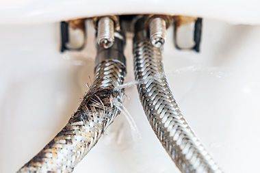 leaking water from damaged braided hoses under a sink showcasing potential 25 plumbing repair issues