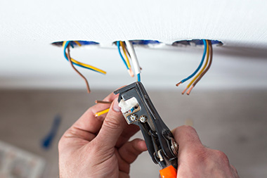 person using wire strippers on electrical wires in a wall for home improvement project safely configuring connections for 23 electrical tasks